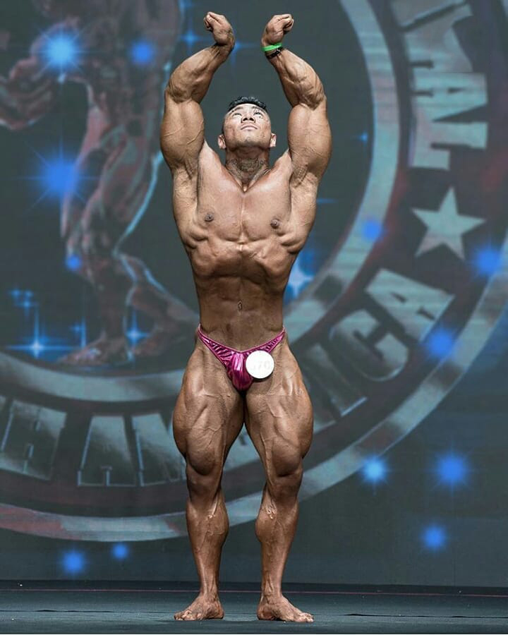 Caio Eiji Sirahata performing a posedown on a bodybuilding stage looking ripped