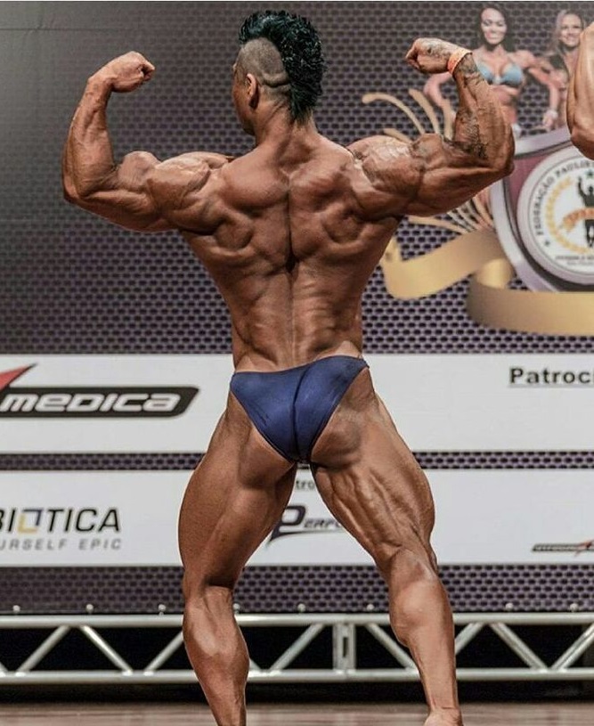 Caio Eiji Sirahata performing a back double biceps flex on the bodybuilding stage