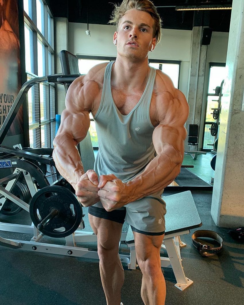 Carlton Loth flexing his muscles in a greyish tank top in the gym