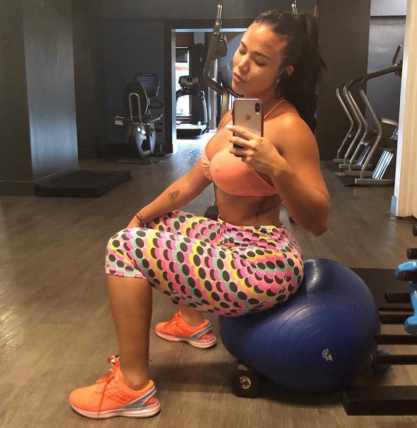 Diana K. Levy taking a selfie in the gym sitting on a medicine ball looking fit