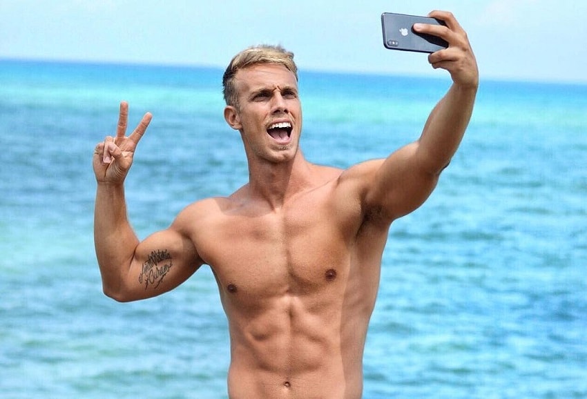 Edoardo Santonocito taking a shirtless selfie outdoors by the sea, looking lean and aesthetic