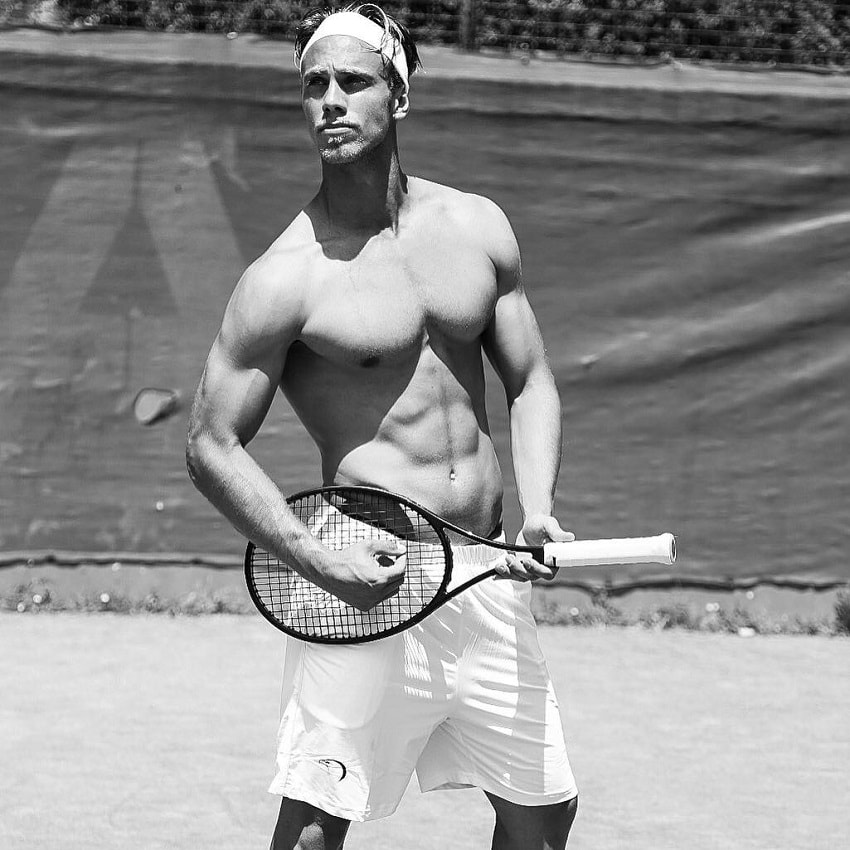 Edoardo Santonocito standing shirtless on a tennis court with a tennis racket in his hand