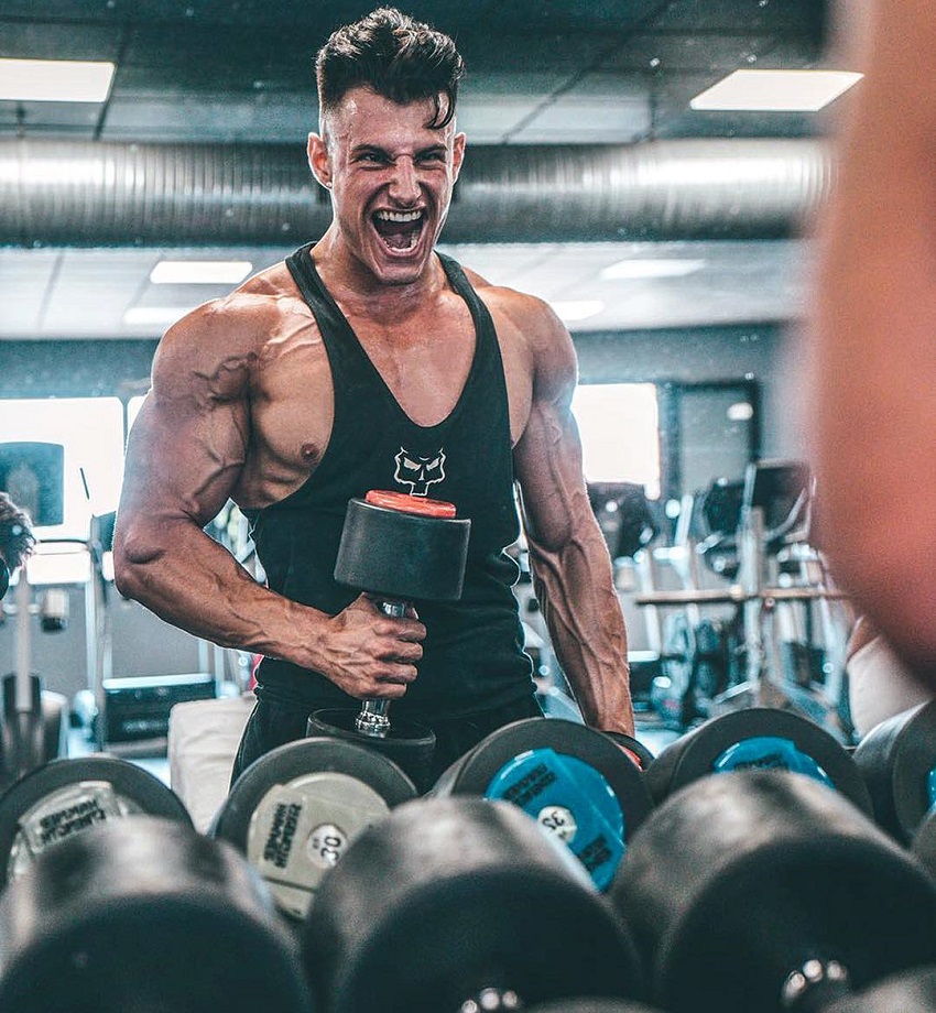 Francesco Della Vedova doing biceps curls while looking at himself in the mirror with a pained grimace