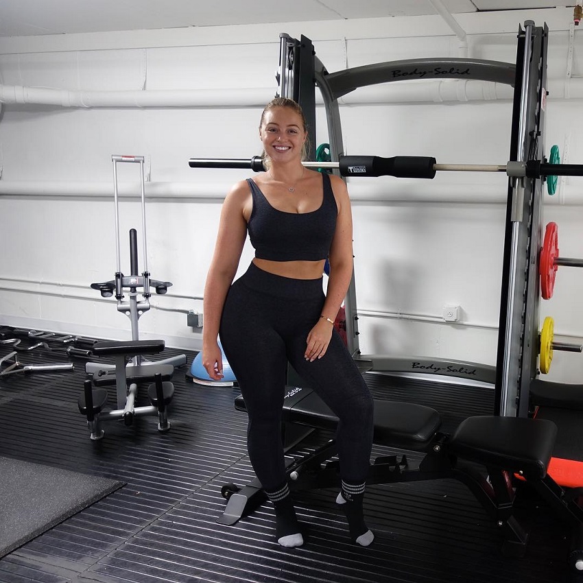 Iskra Lawrence posing in the gym next to weights looking fit and happy