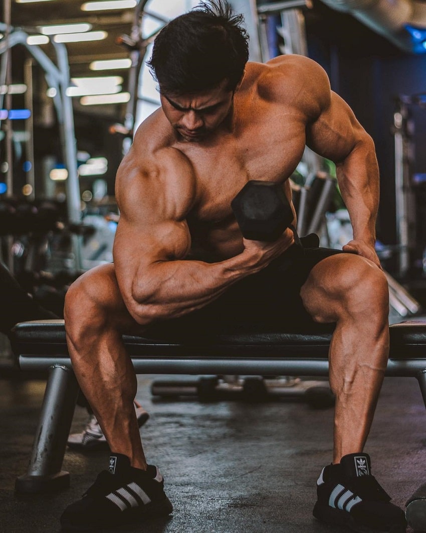 Ismael Martinez performing dumbbell biceps curls seated on a bench while being shirtless