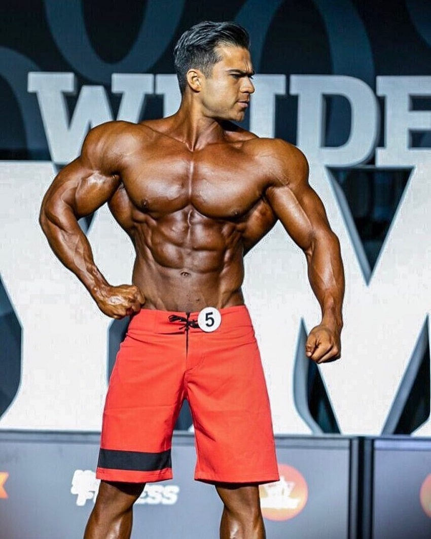 Ismael Martinez posing on the Joe Weider's Mr. Olympia Men's Physique stage, looking ripped and muscular