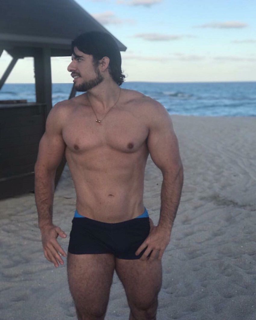 Lucas Giovani standing shirtless on the beach looking fit and lean