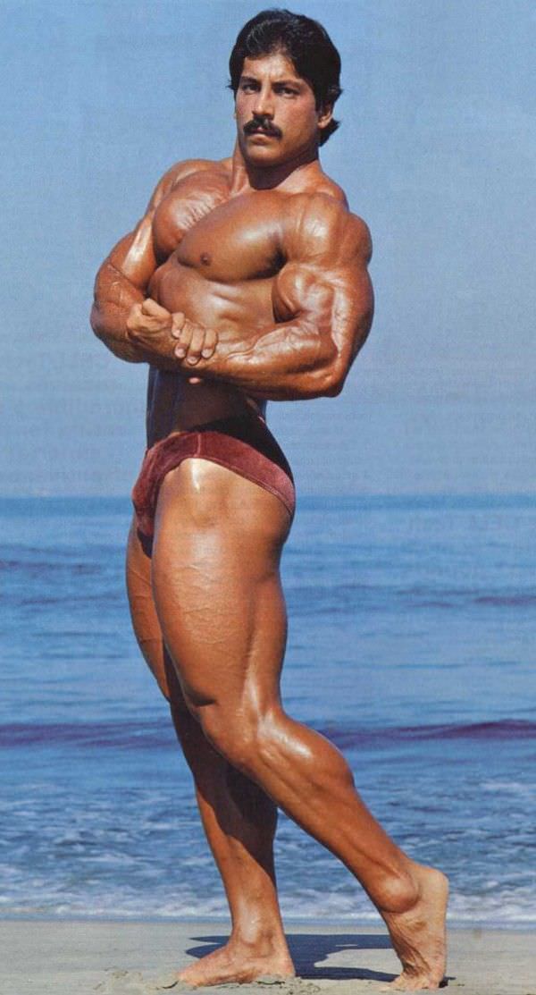 Ray Mentzer doing a shirtless side chest pose during a sunny day on a beach