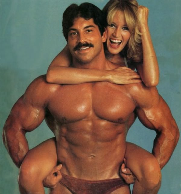 Ray Mentzer holding a woman in a photo shoot looking ripped