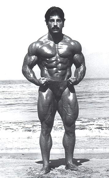 Ray Mentzer posing shirtless on the beach in a black and white photo, looking muscular and ripped