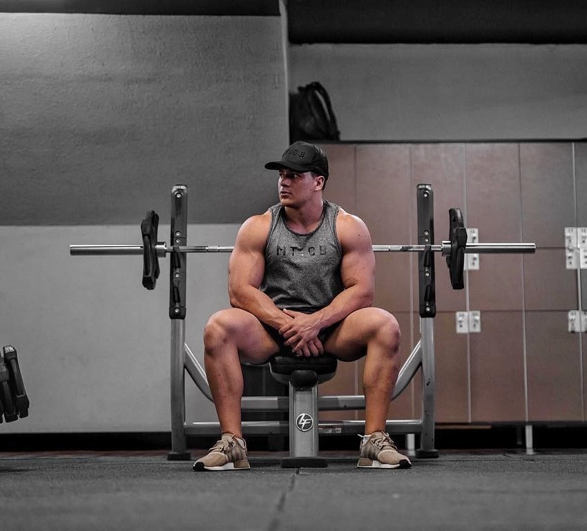 Caio Bottura sitting on the bench in the gym looking swole and muscular