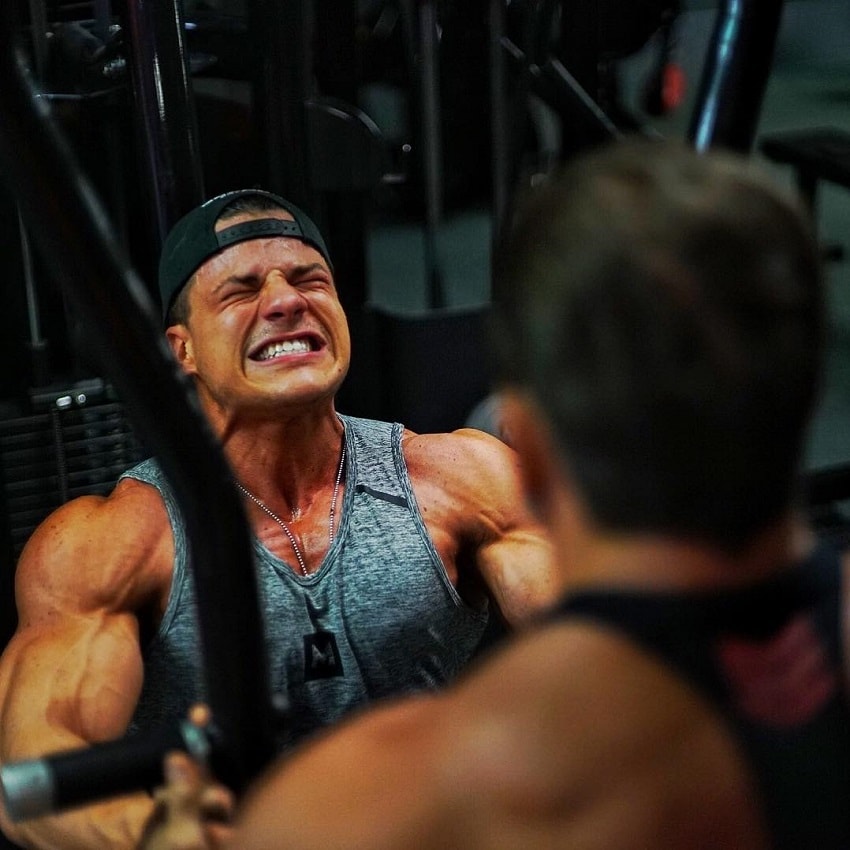 Caio Bottura doing heavy chest machine press in the gym having a pained grimace