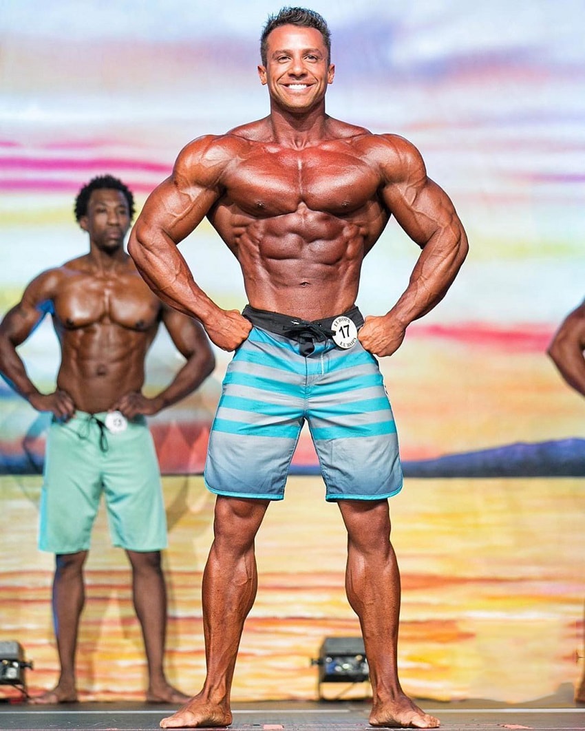 Diogo Montenegro posing on the Men's Physique stage, showcasing his ripped chest, arms, and midsection