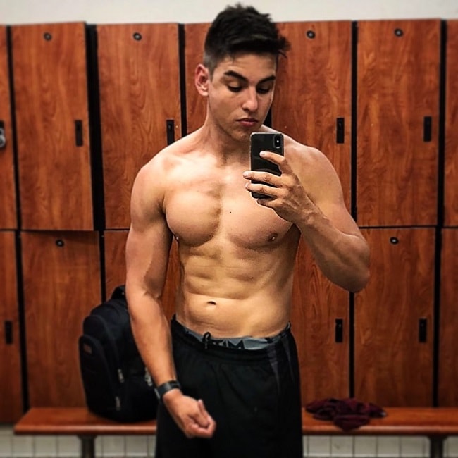 Gabriel Arones taking a selfie of his shirtless muscular body in a gym locker room