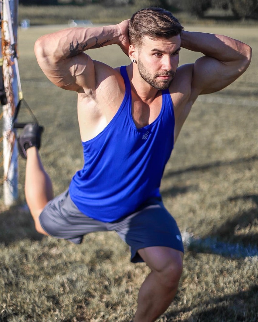 Jake Burton training outdoors in a blue tank top looking vascular and ripped