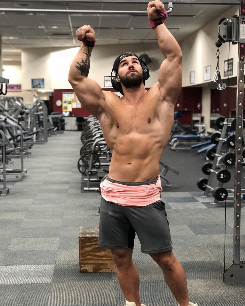 Jake Burton flexing his muscles shirtless in the gym looking up at the ceiling