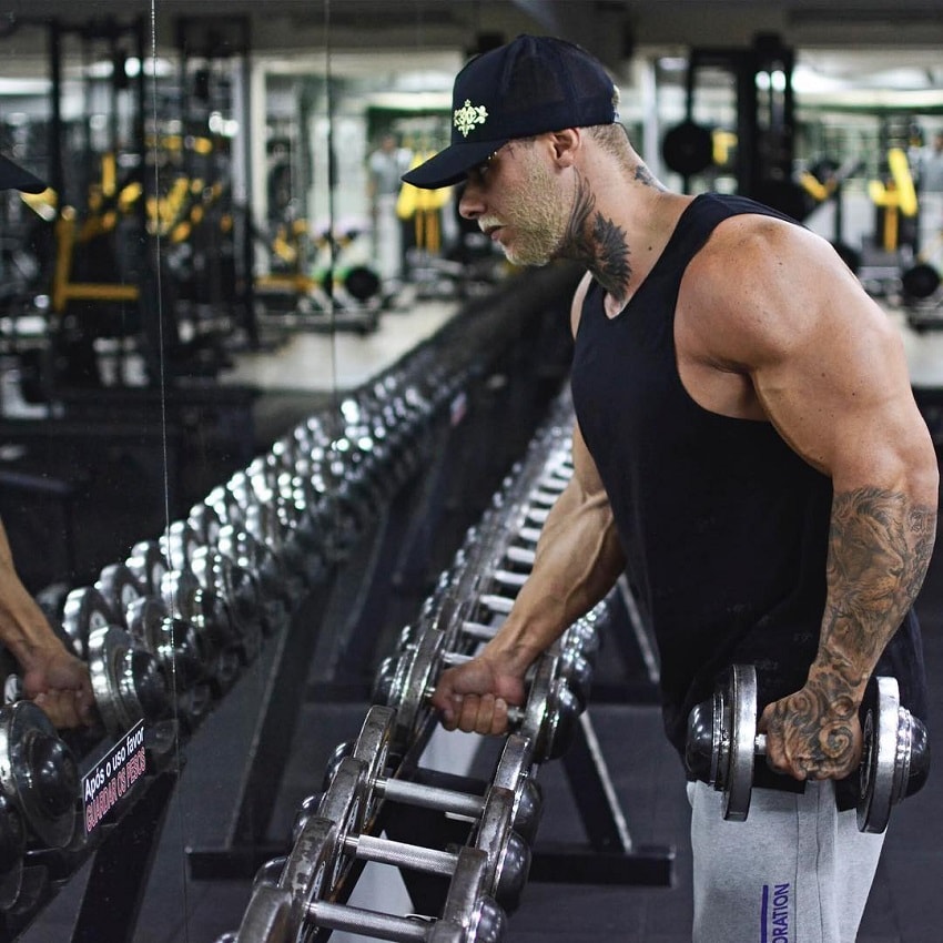 Leo Stronda doing dumbbell rows by the dumbbell rack in the gym