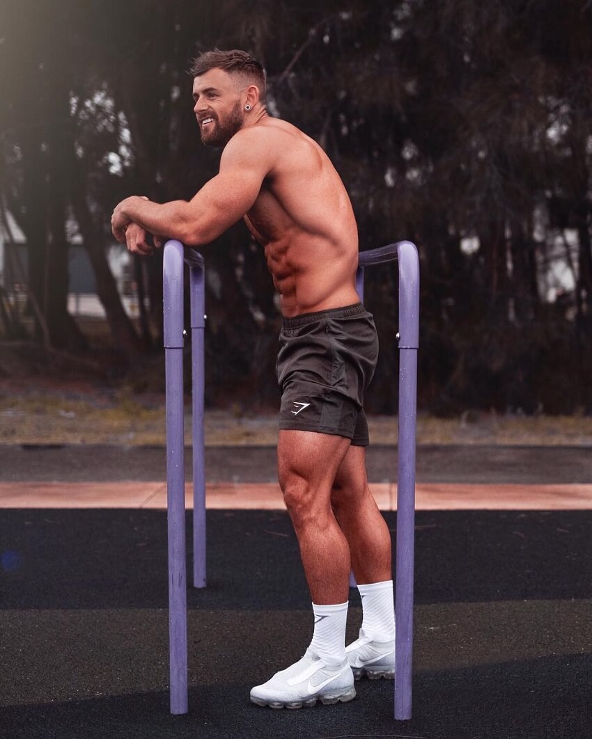 Nathan McCallum resting shirtless on a calisthenics playground