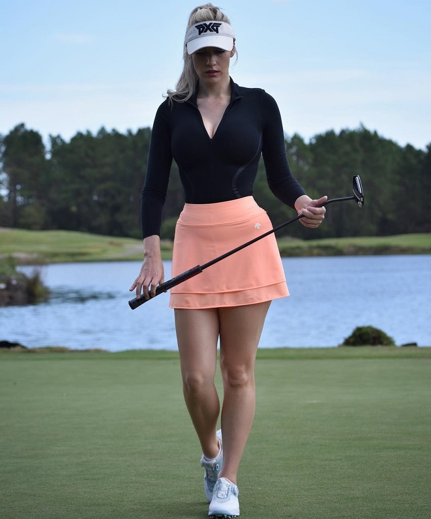 Paige Spiranac walking down the golf court with a golf club in her hands