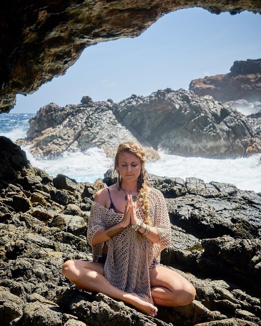 Rachel Brathen doing meditation on rugged rocks by the sea