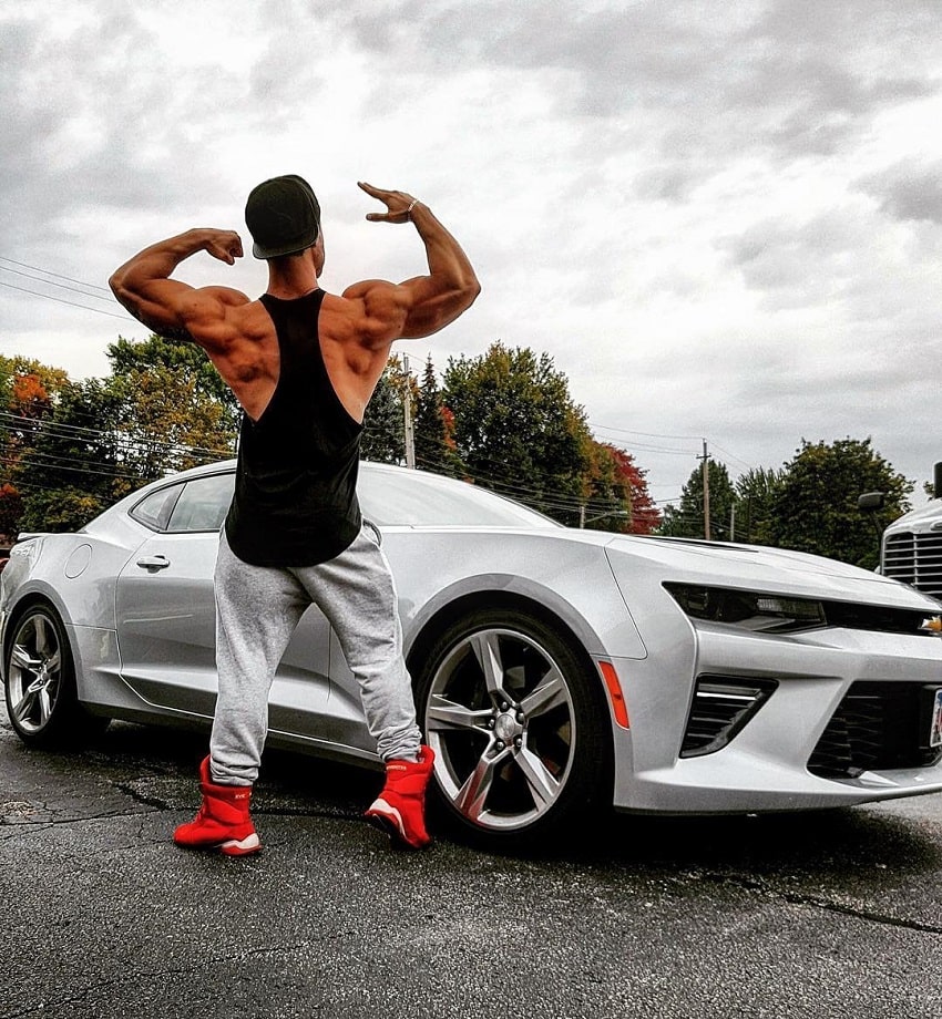 Rafael Rey standing by a new white sports car, flexing his back muscles