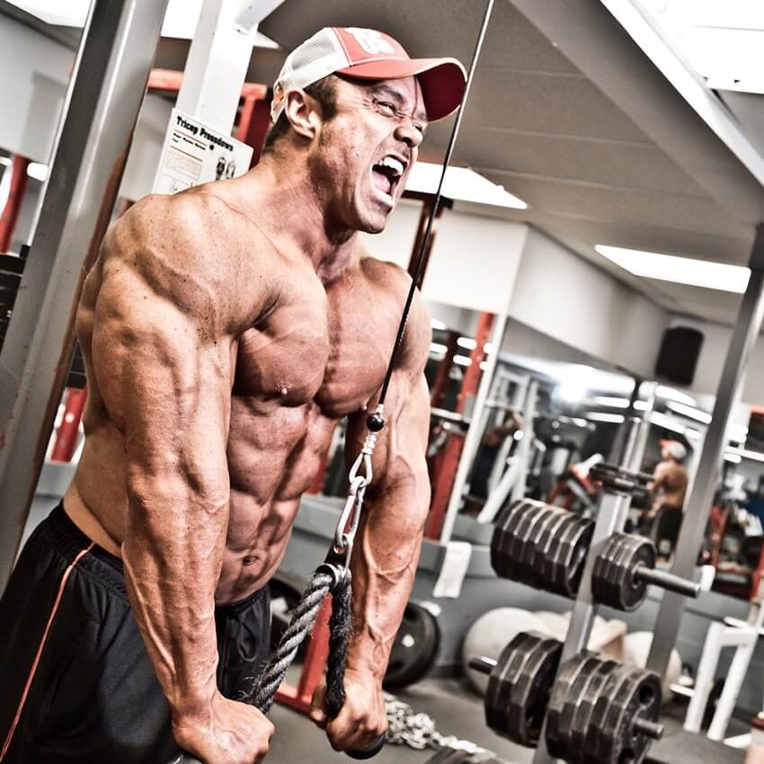 Ron Partlow doing triceps extensions in the gym with a pained expression on his face