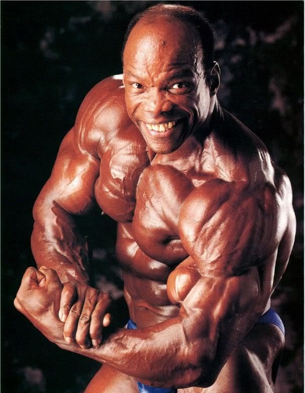 Albert Beckles flexing his ripped arms in a bodybuilding photo shoot