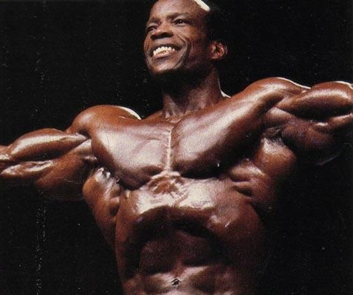Albert Beckles spreading his arms wide in front of an audience on the bodybuilding stage