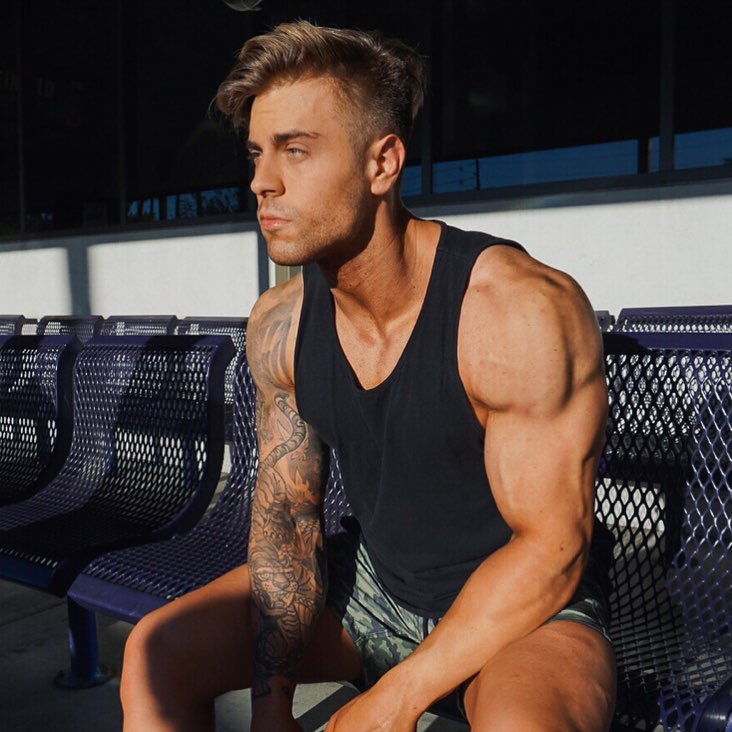 Andre Habowsky sitting in a chair, wearing a black tank top, looking ripped and muscular