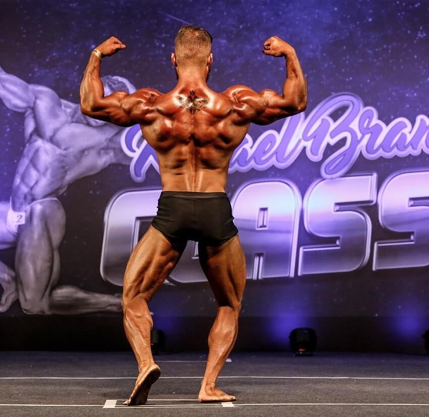 Caique Meirelles performing a back double biceps pose on the bodybuilding stage