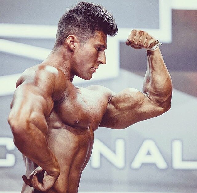 Caique Meirelles flexing his biceps on a bodybuilding stage