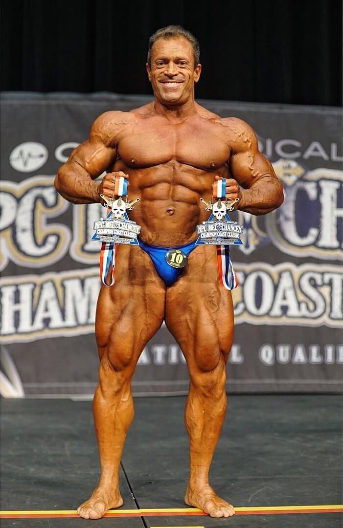 Fernando Sardinha posing on the bodybuilding stage with a trophy