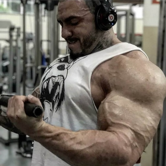 Matheus Donaire doing cable curls in the gym, looking ripped and huge