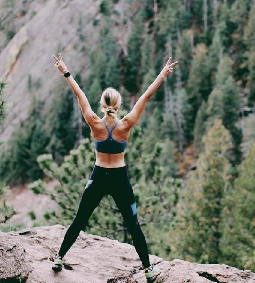 Natalie Uhling standing on a cliff overlooking a forest with her arms spread wide