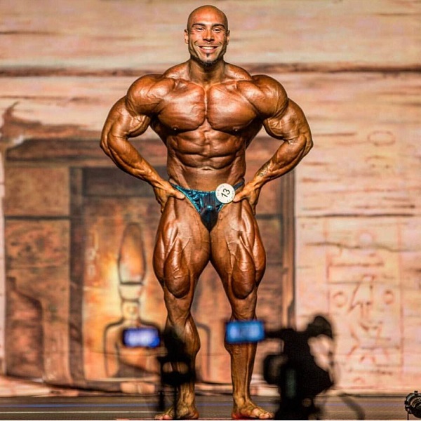 Samir Troudi flexing in a bodybuilding competition in front of cameras and an audience