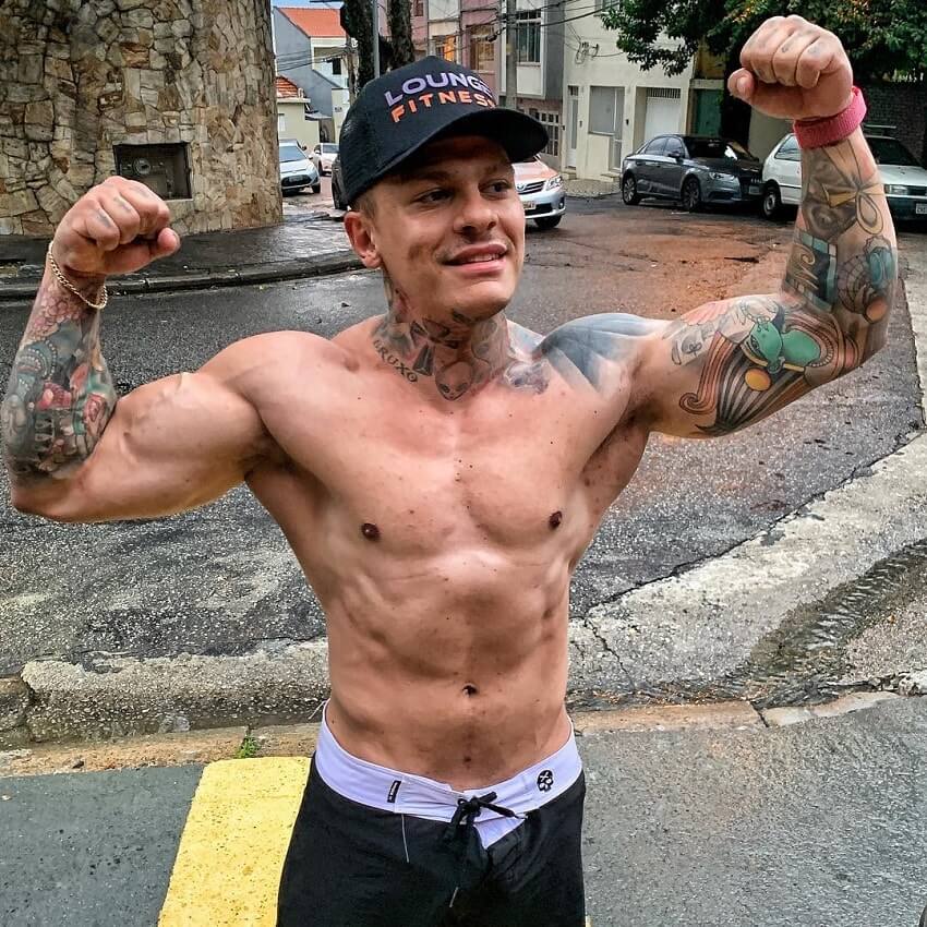 Tiago Toguro doing a shirtless front double biceps pose on the street