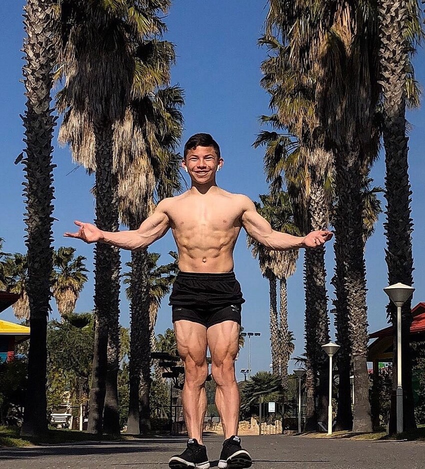 Tristyn Lee posing shirtles next to palm trees.