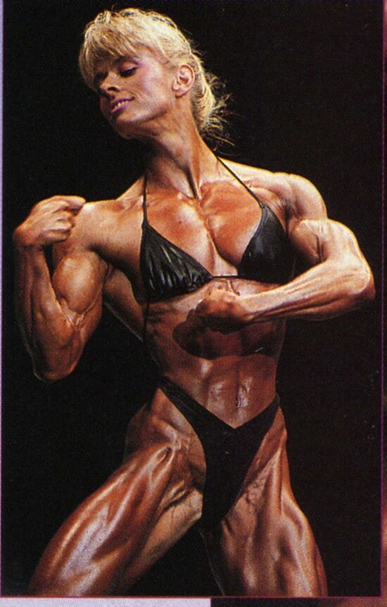 Anja Schreiner posing on the bodybuilding stage displaying her conditioned and muscular physique