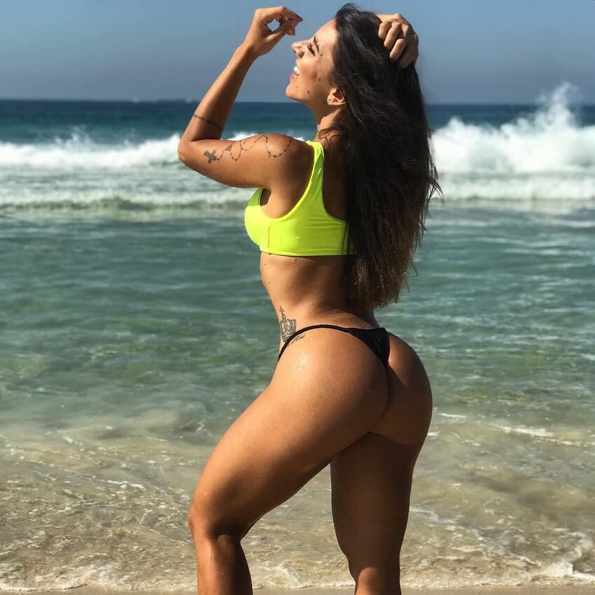 Fabriny Storck standing on a beach in a bikini, with her glutes and legs looking awesome