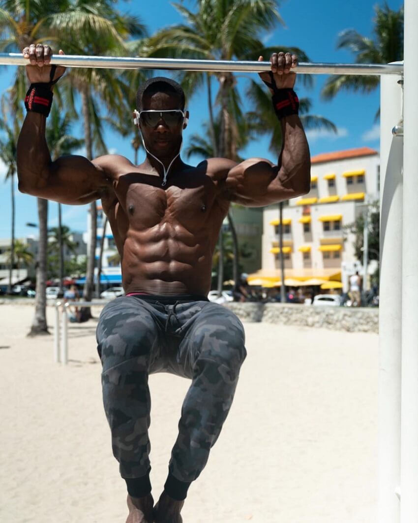 Max Philisaire doing pull ups shirtless on the Miami beach, looking extremely ripped