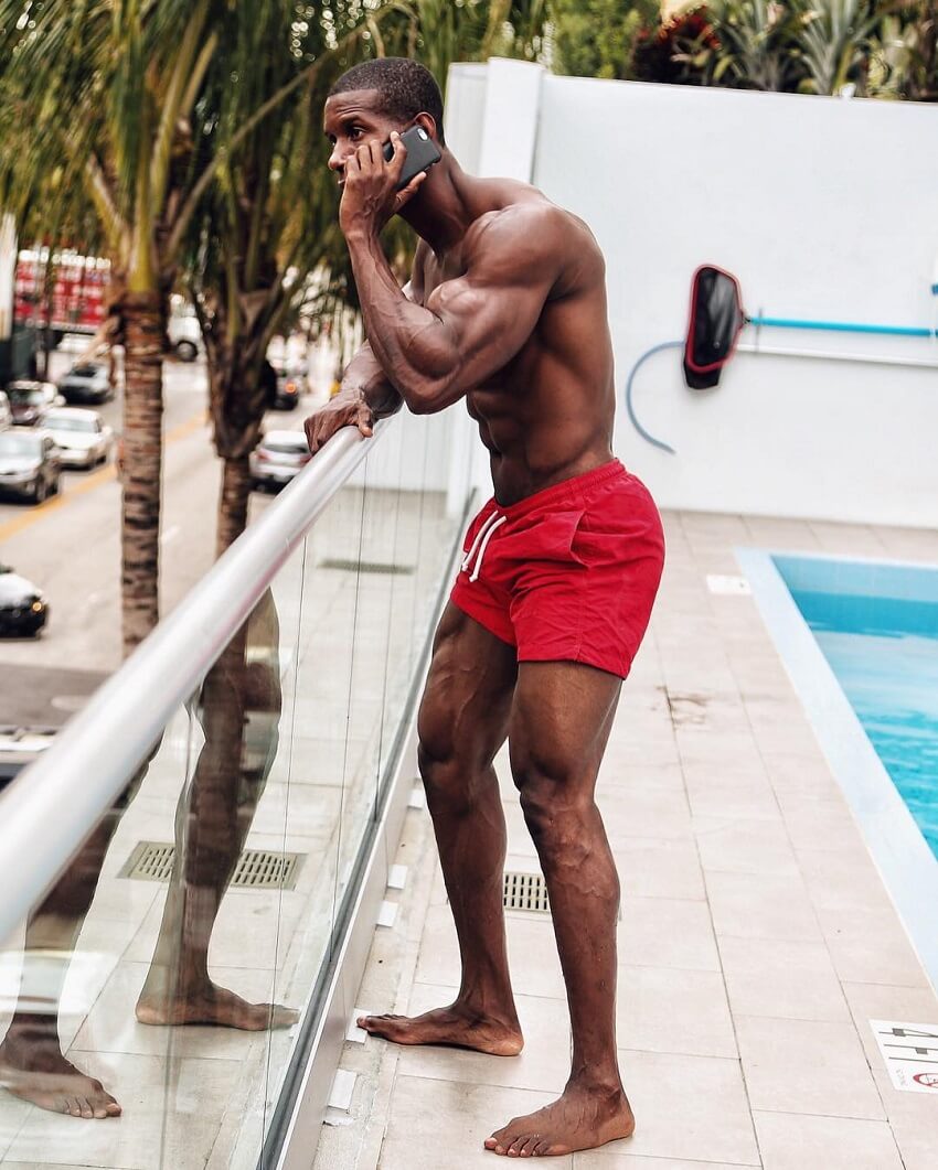 Max Philisaire standing shirtless by the pool, talking on the phone