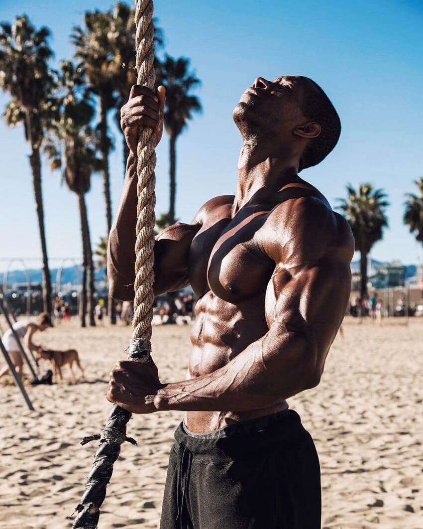 Max Philisaire standing shirtless on the beach pulling a rope and looking up