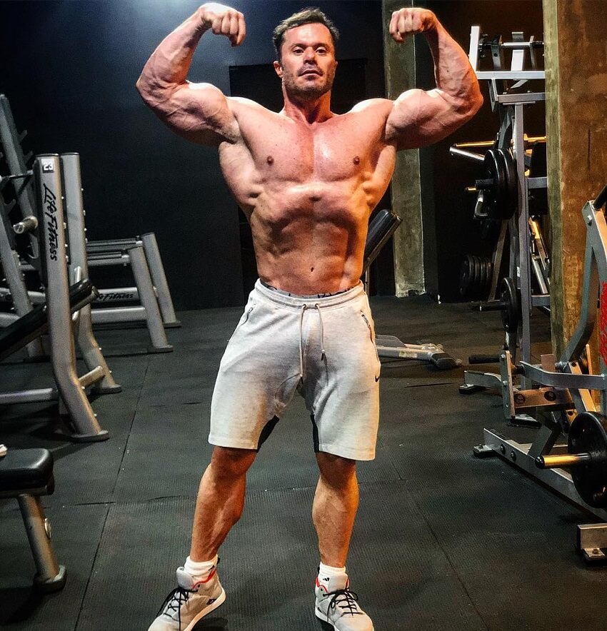 Renato Cariani flexing his arms while being shirtless in the gym