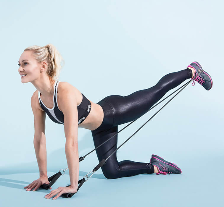 Simone De La Rue doing glute kicbacks with resistance bands