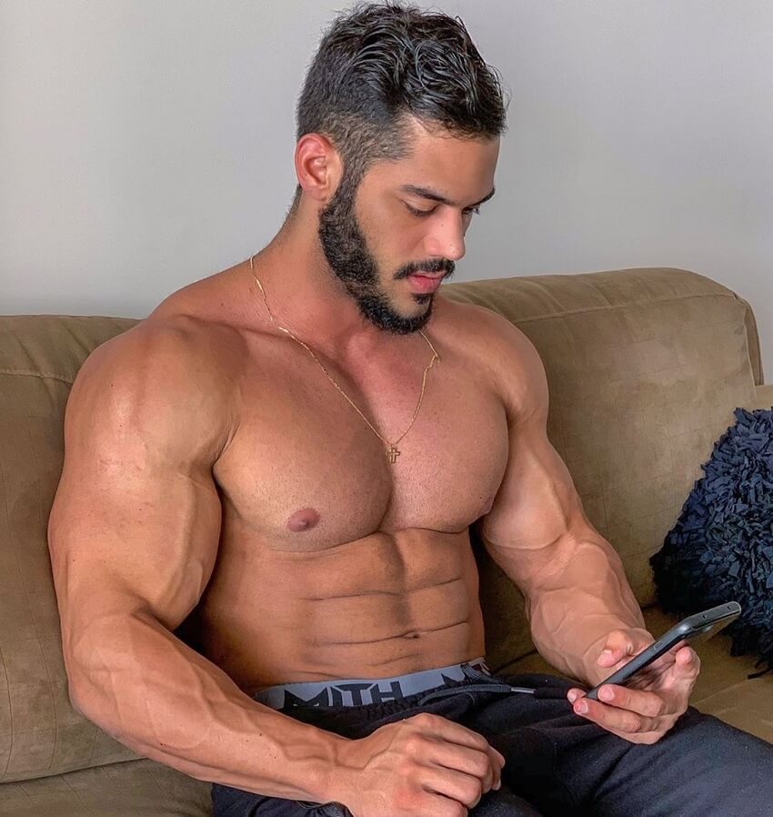 Geder Rocha sitting shirtless on a couch, texting on his phone, looking ripped and muscular