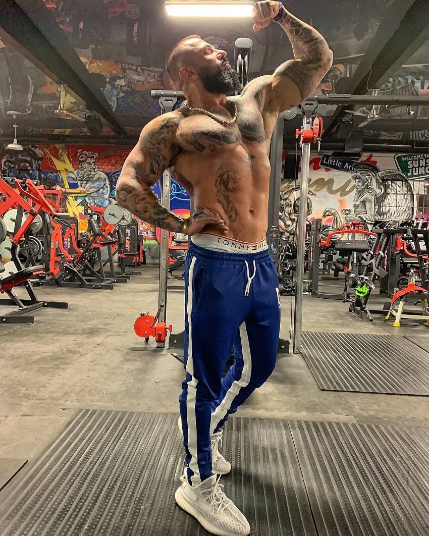 Jack Torosian flexing his biceps shirtless in the gym