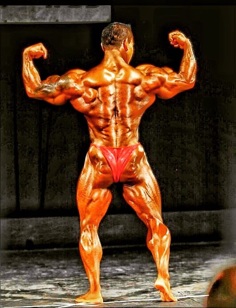 Kris Dim hitting a back double biceps pose on the bodybuilding stage