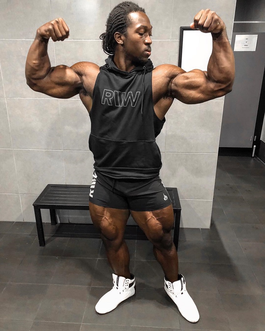 Kwame Duah flexing front double biceps in a black tank top