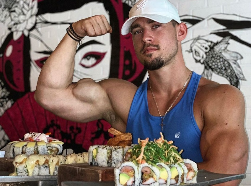 Jordan Strickland flexing his bulging biceps while sitting at a dinner table with food