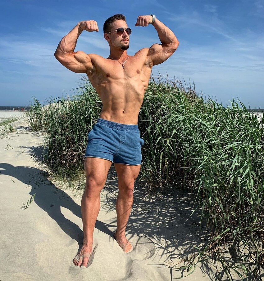 Jordan Strickland flexing front double biceps on the beach shirtless